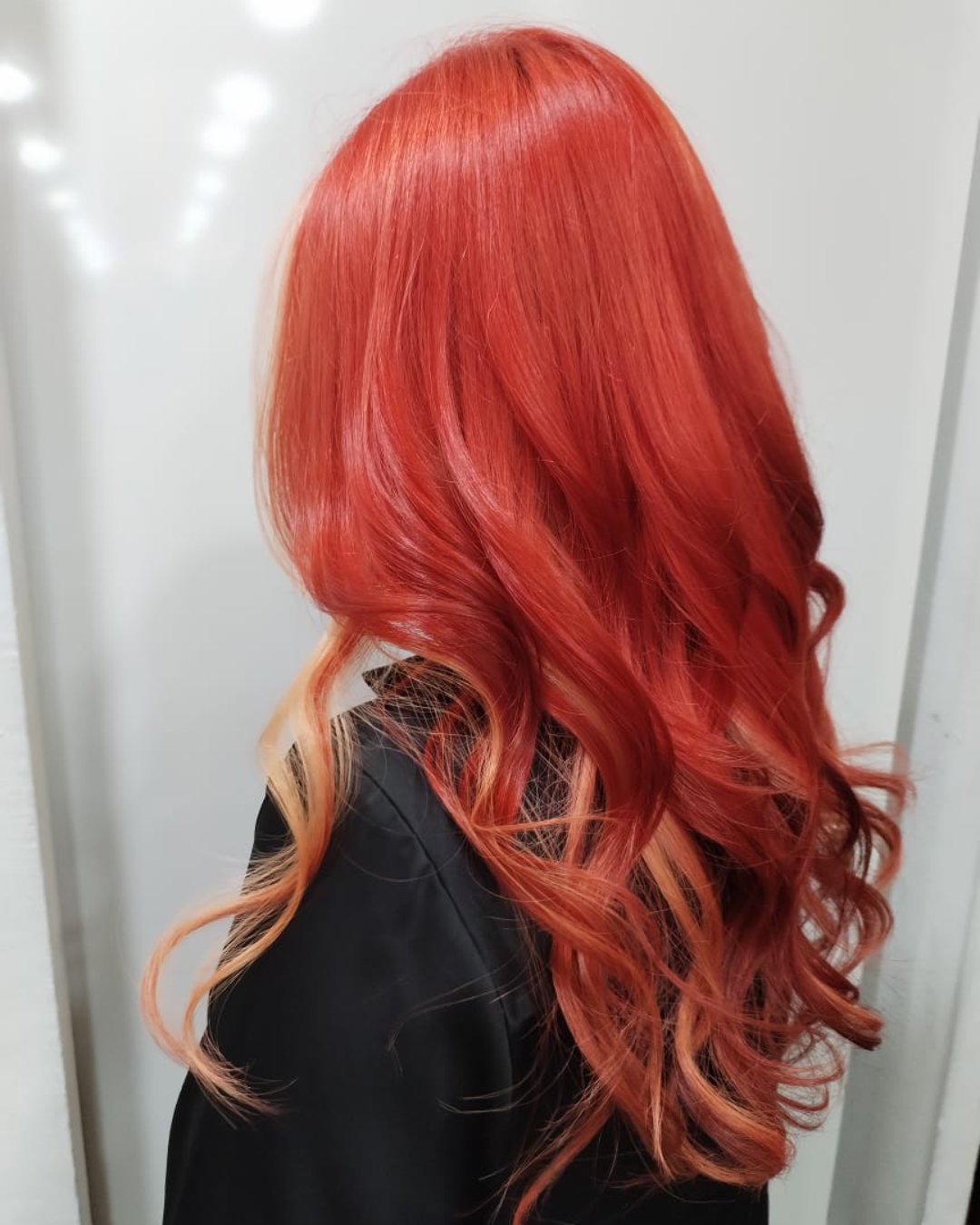 The side profile of a woman's long hair coloured in bright red and styled with curls