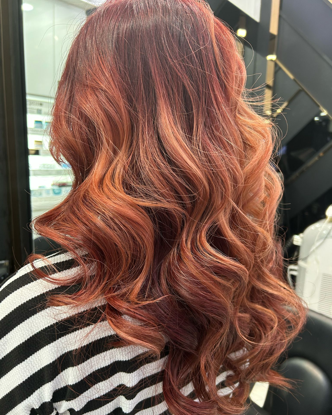 The back profile of a woman's long hair coloured in copper orange and styled in curls